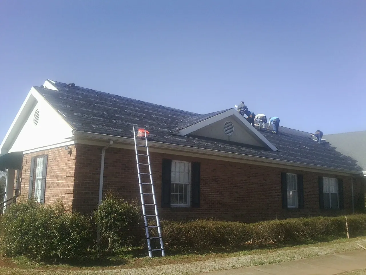 Crew tearing shingles off a brick ranch roof with a ladder set — Emergency Roof Repair work by our crew in Sanbornville