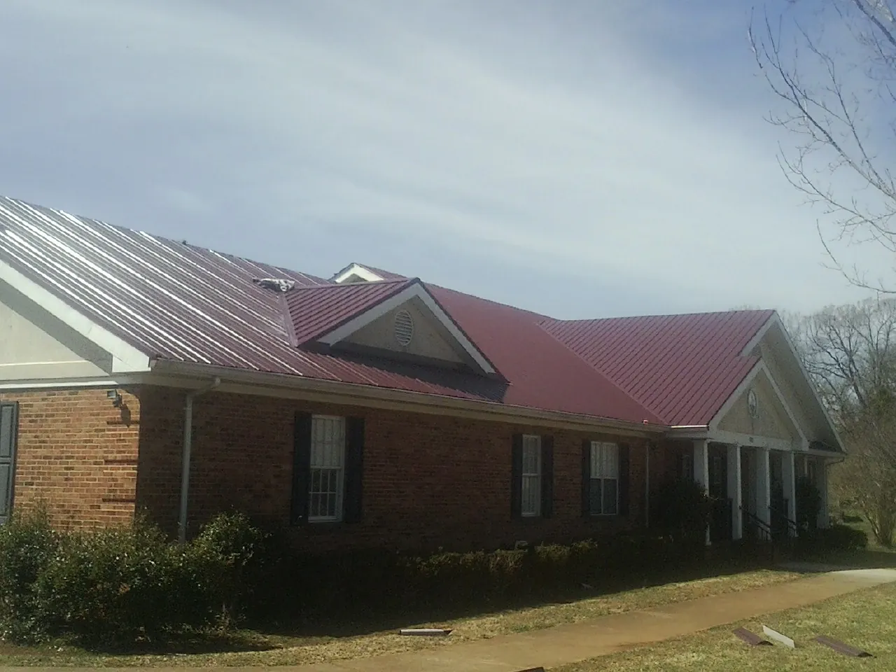 Red metal roof with gabled entries on a long brick building, from a Hail Damage Roof Repair job in Sanbornville