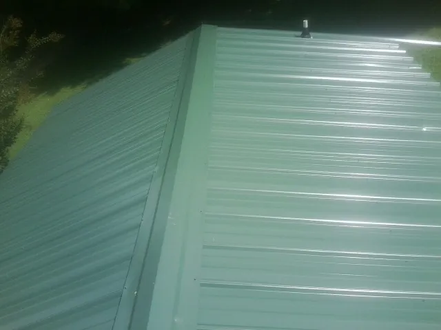 New green metal panels meeting at the ridge of a roof — Flat Roof Repair work by our crew in Sanbornville
