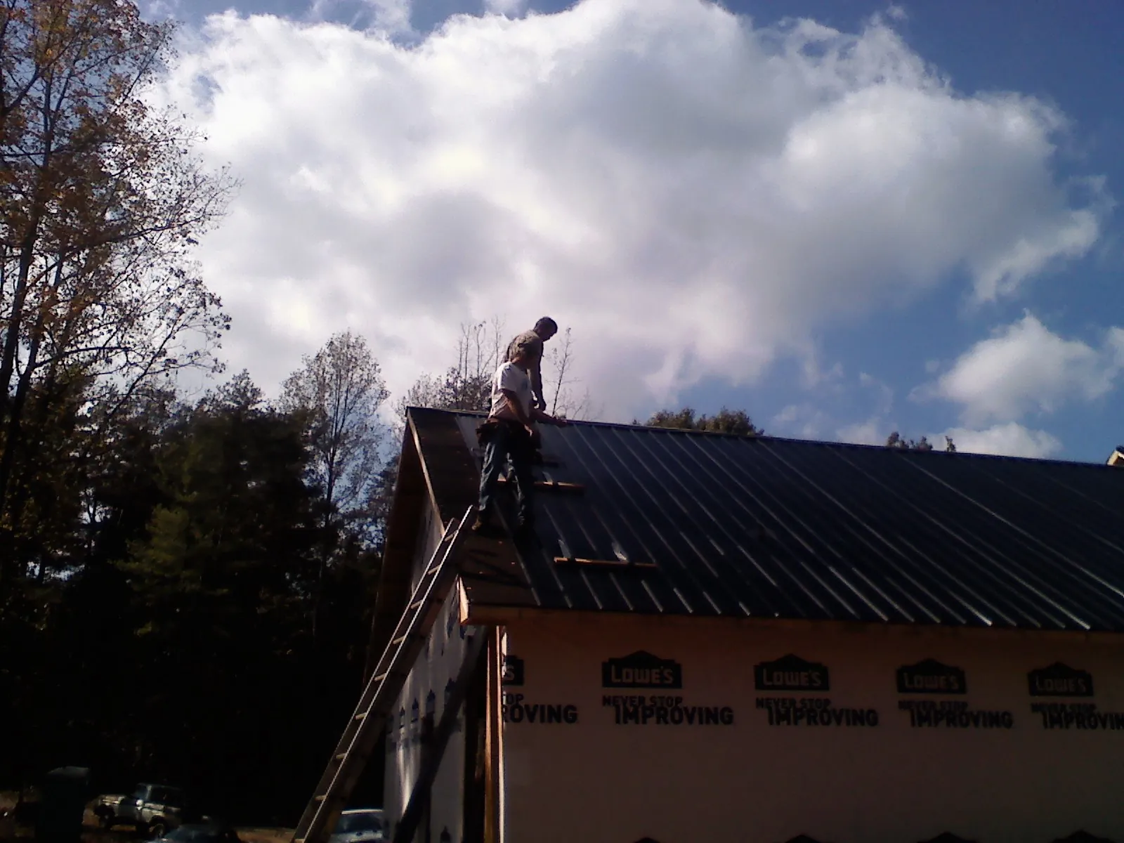 Roofer fastening dark metal panels high against a cloudy sky, from a Roof Inspection job in Sanbornville