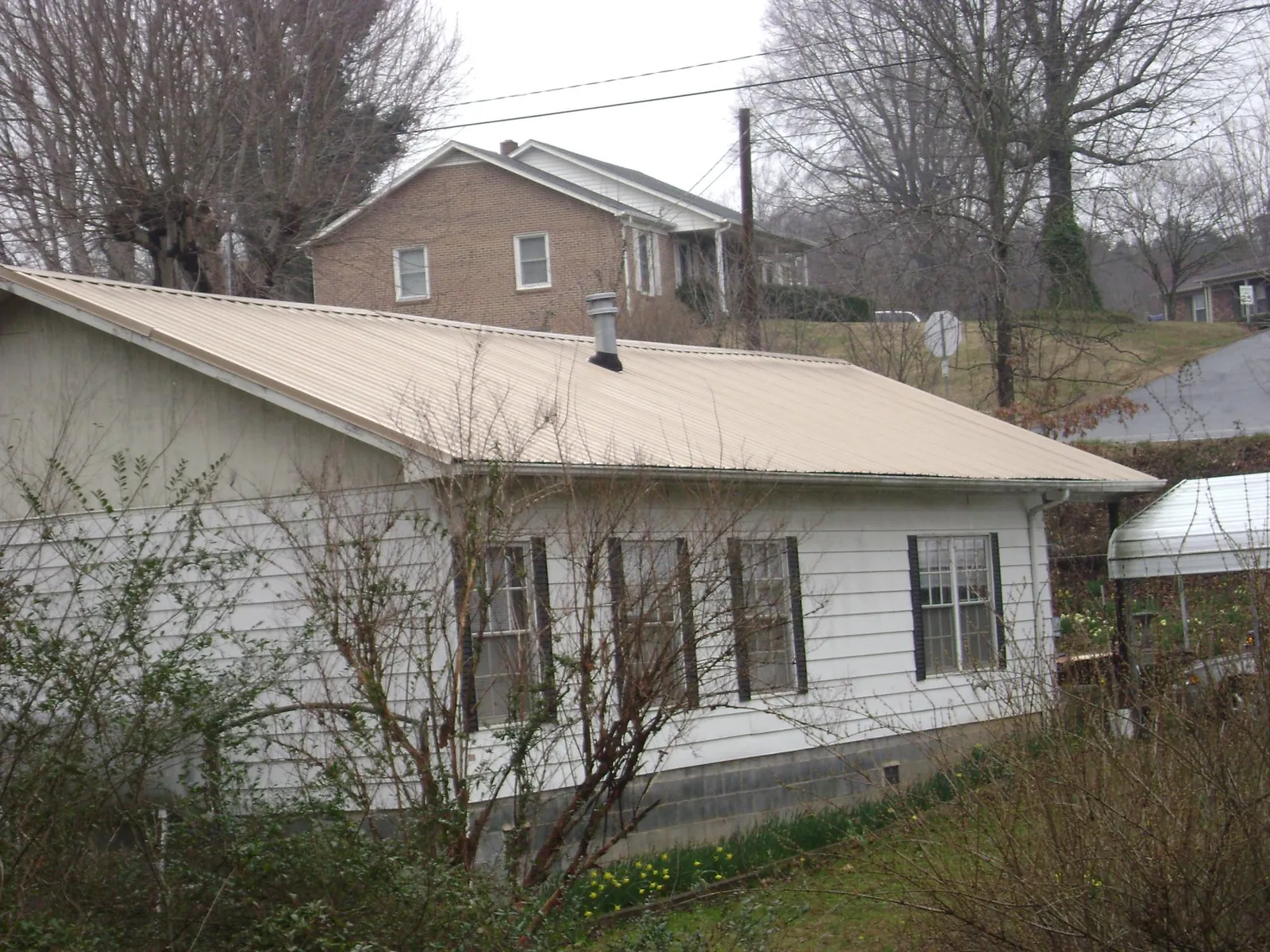 Tan metal roof on a white sided house set into a hillside — Commercial Roofing by Roofing Brothers in Sanbornville