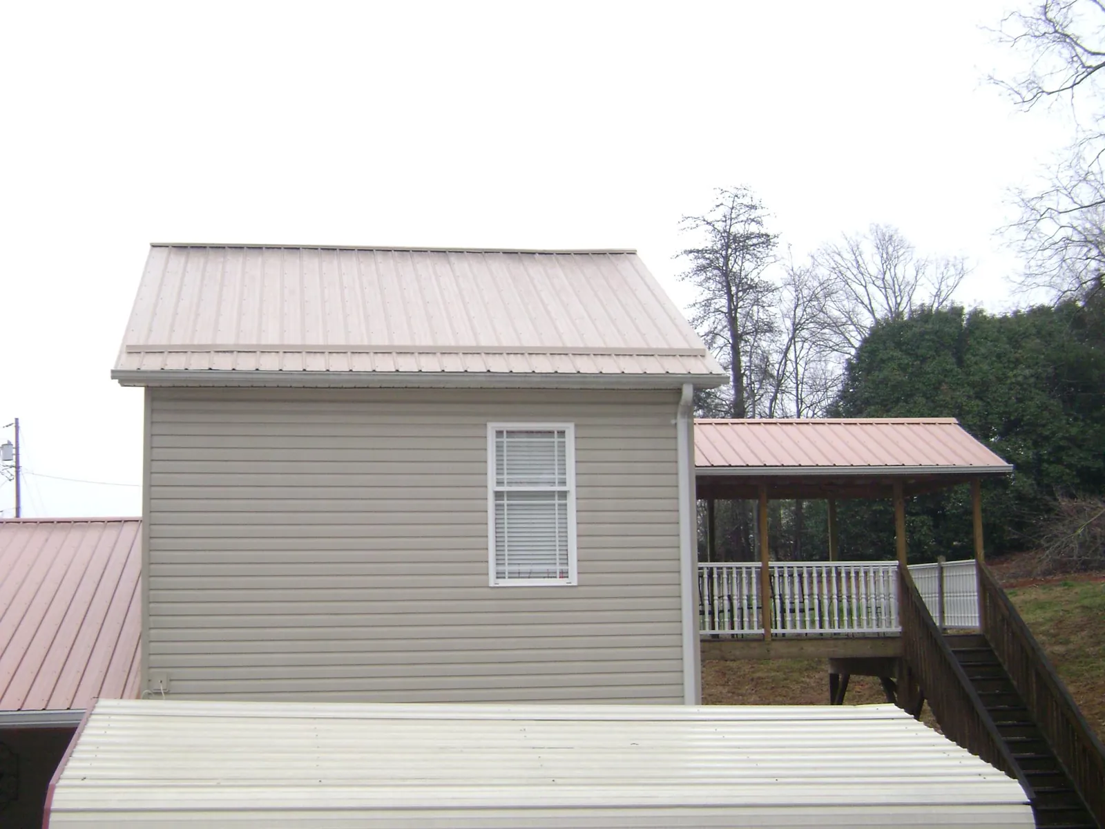Tan metal roofs on a two story addition and attached porch, from a Roof Replacement job in Sanbornville